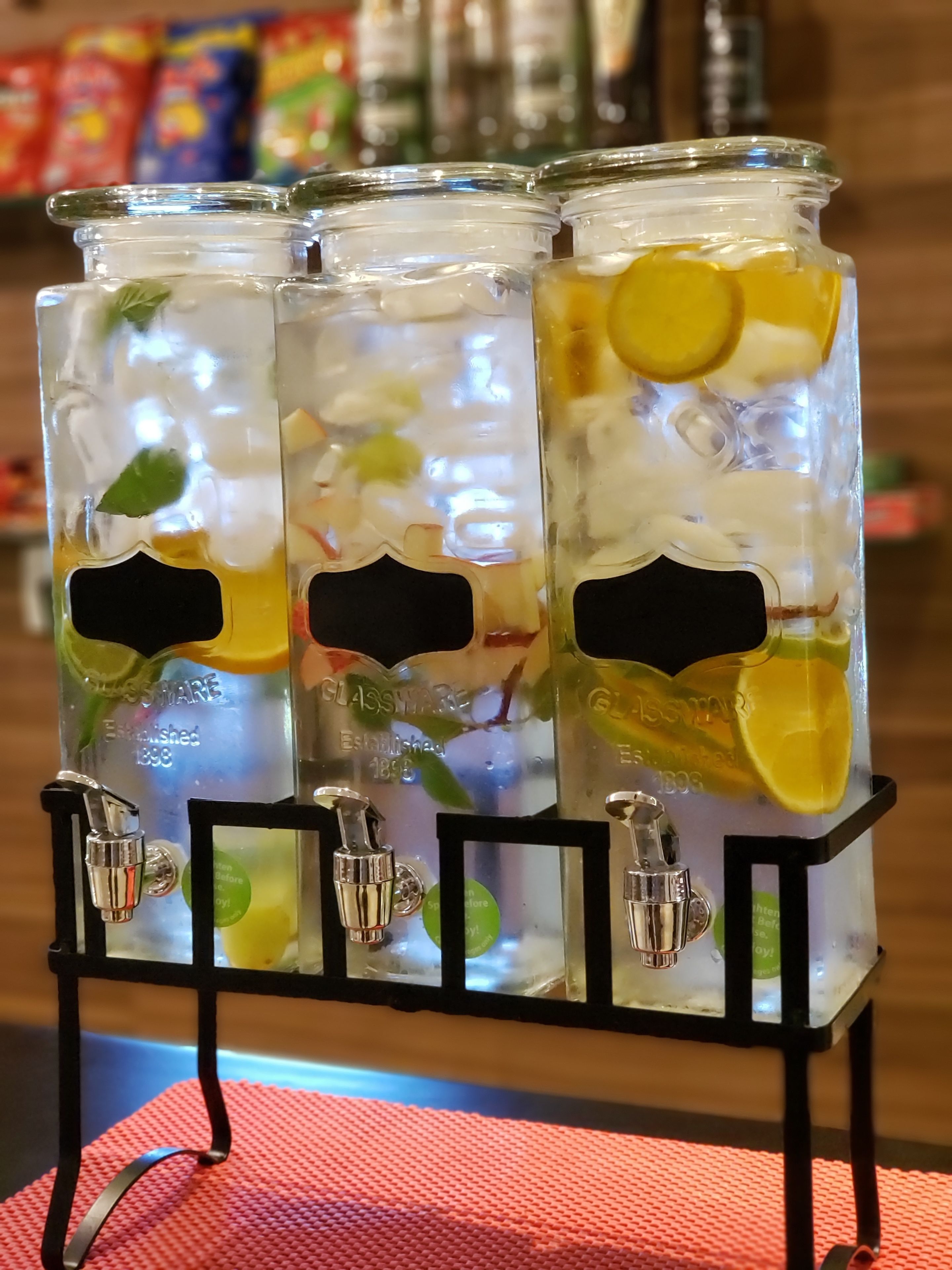 Three glass jars with ice and fruit slices on a black stand.