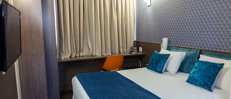 A hotel room with a bed, a desk, an orange chair, and a television.