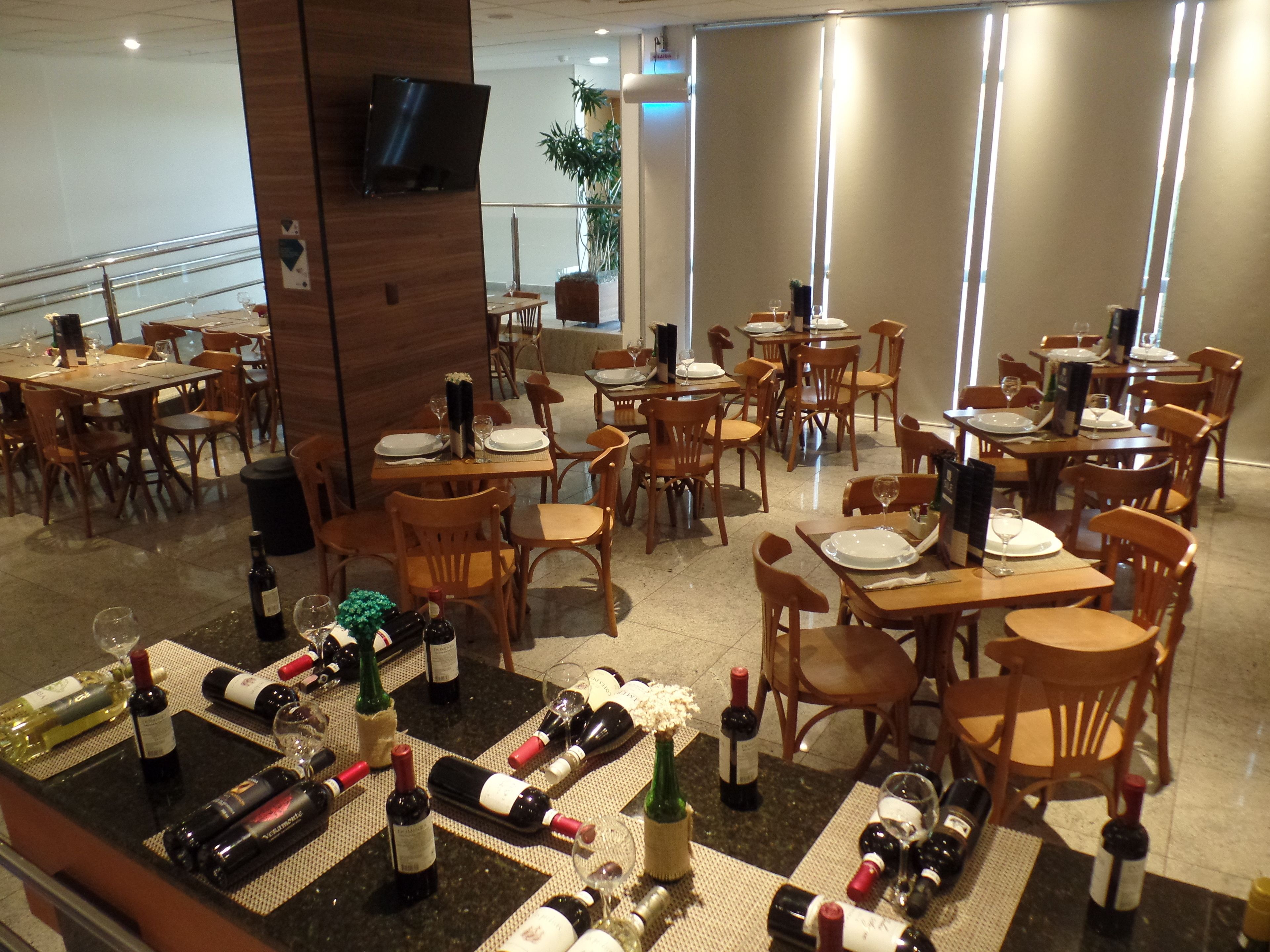 A restaurant with multiple tables and chairs, some with wine bottles and glasses on them.