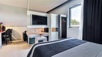 Una habitación de hotel moderna con una cama grande, un escritorio con silla, un televisor montado en la pared y una ventana con cortinas.