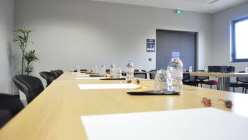 Un salón de conferencias con una larga mesa, sillas, botellas de agua y una planta en maceta.