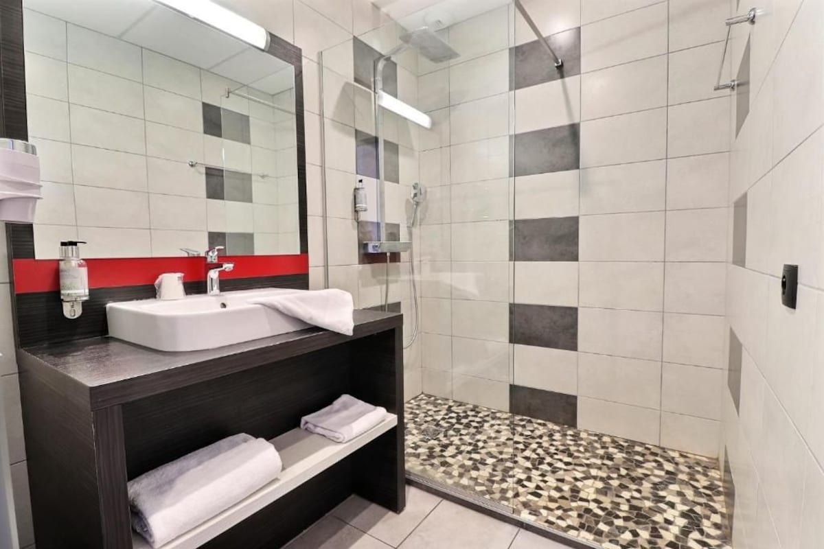 Un baño moderno con ducha envuelta en vidrio, un lavamanos blanco y una pared de acento roja.