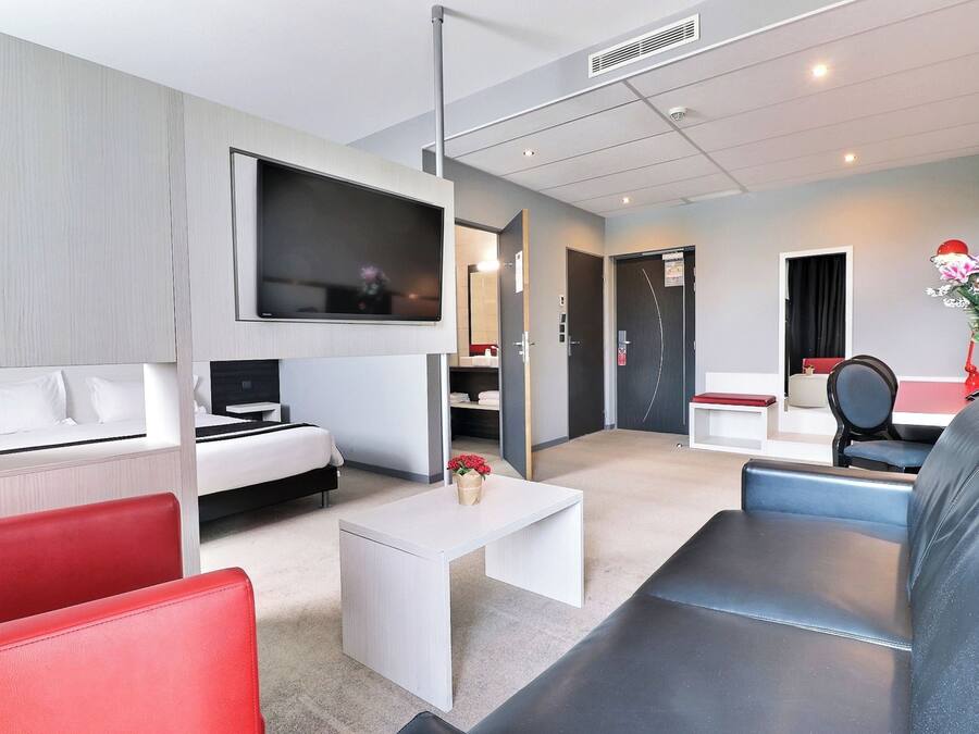 A modern hotel room with a bed, a TV, a desk, and seating areas.