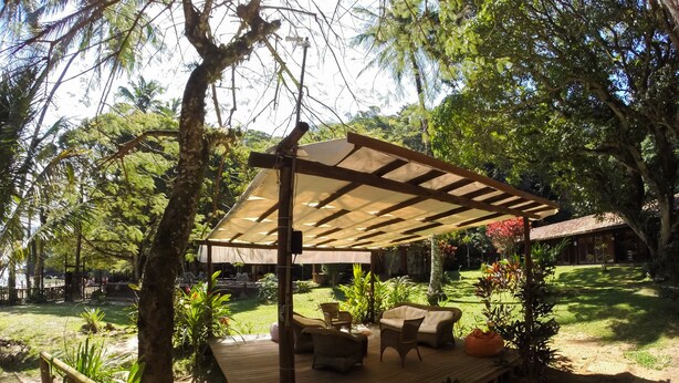 A wooden deck with outdoor furniture, surrounded by lush greenery and a pergola providing shade. - Pousada Praia da Crena (Angra dos Reis)