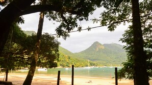 A beach with a wooden deck, a view of the sea, and a mountain in the background. - Pousada Praia da Crena (Angra dos Reis)