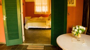 A room with a bed, a table with a vase of flowers, and green shutters on the doors. - Pousada Praia da Crena (Angra dos Reis)