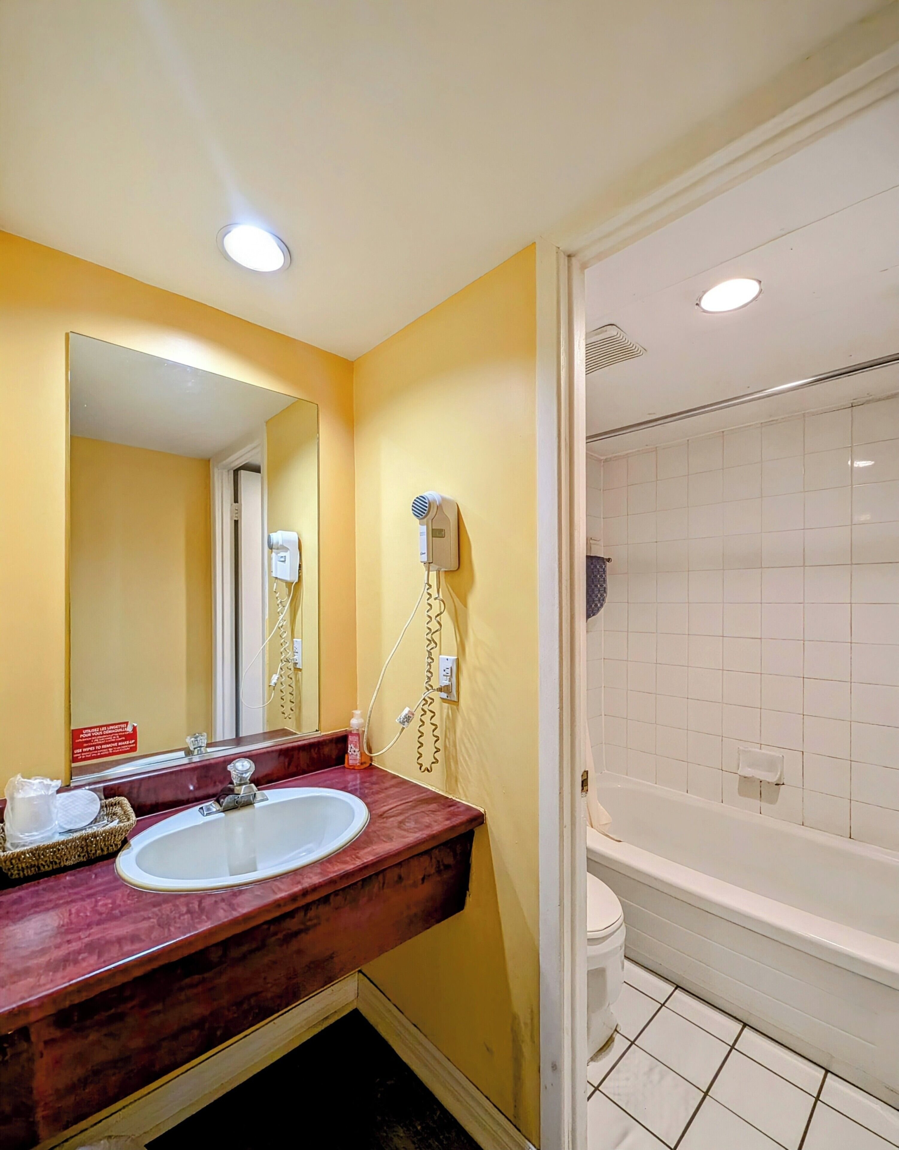 A bathroom with a marble sink, a hairdryer mounted on the wall, and a white bathtub.