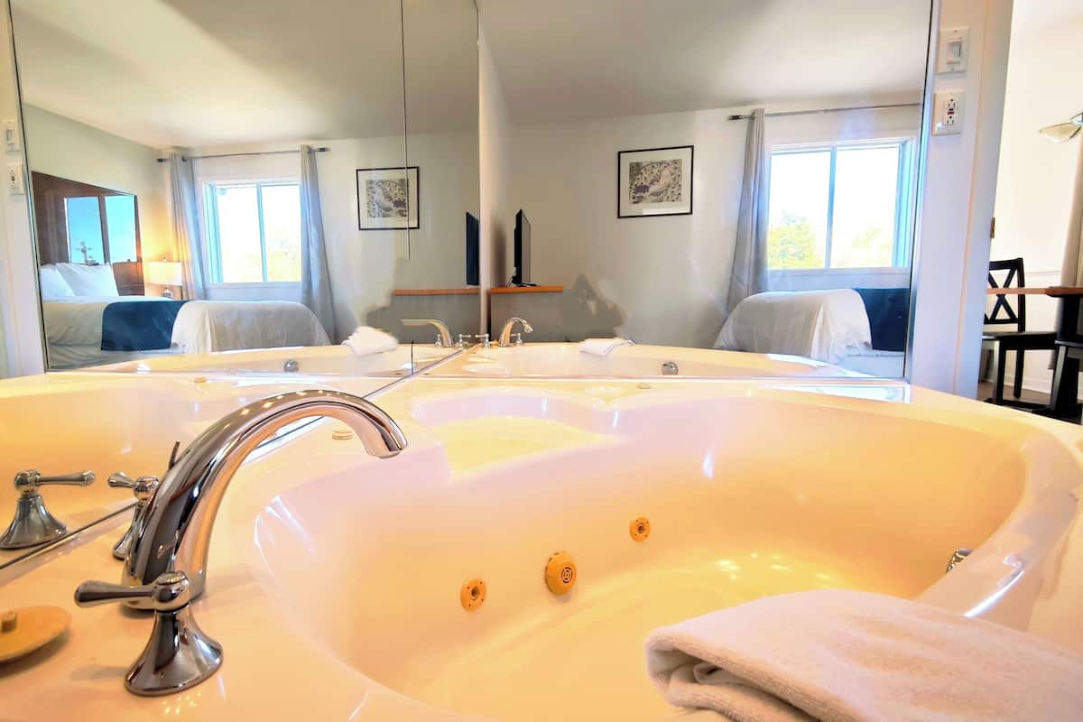 Une salle de bain avec une grande baignoire, un miroir et une fenêtre.