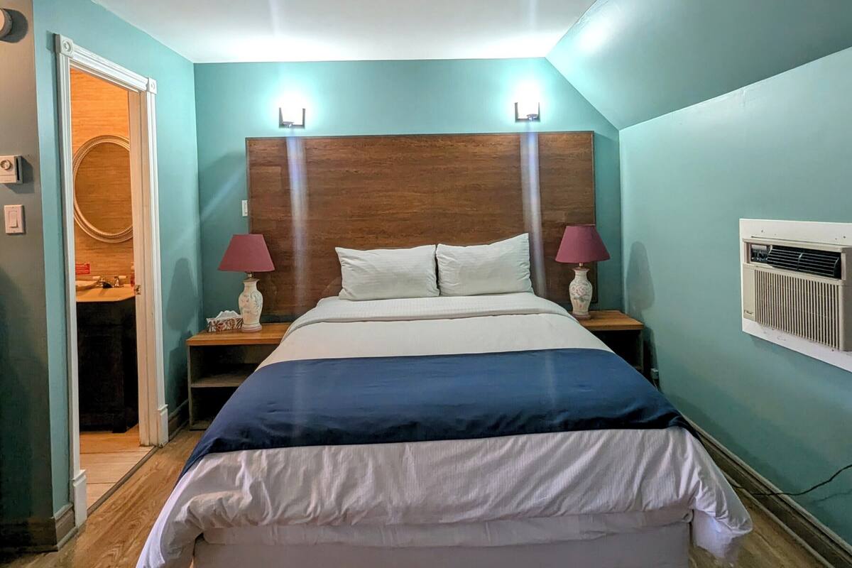 Une chambre à coucher avec une tête de lit en bois, deux lampes de chevet, un lit avec une literie blanche et bleue, et un plancher en bois.
