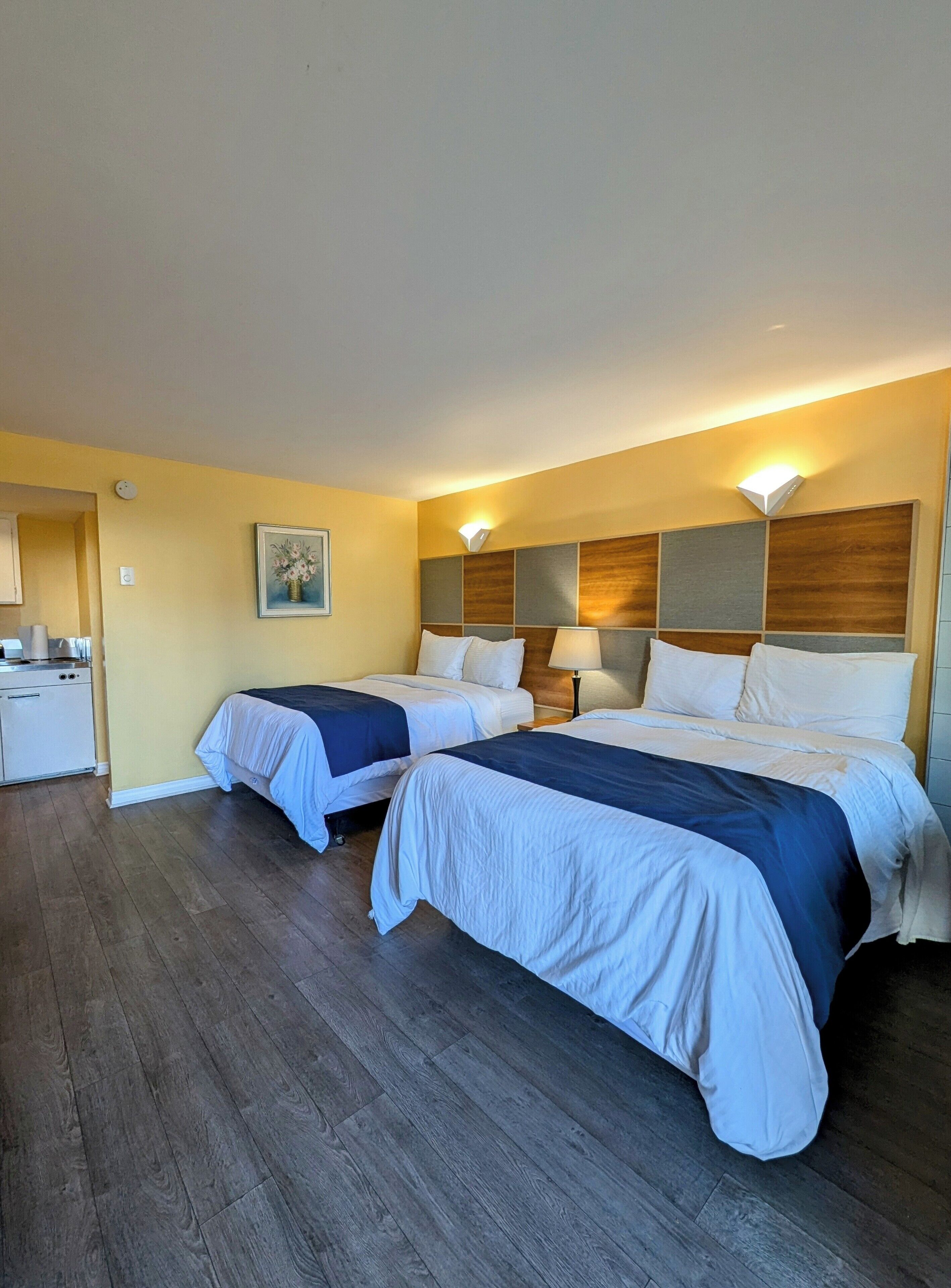 Una habitación de hotel con dos camas, una kitchenette pequeña y un cuadro en la pared.