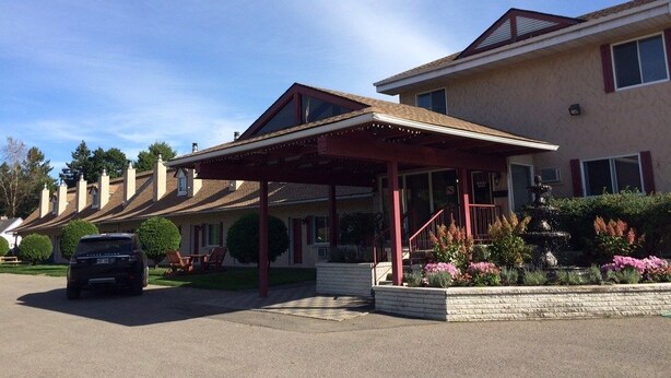 A hotel with a covered entrance, a landscaped garden with a fountain, and a parked car. - Motel des Pentes et Suites (Saint-Sauveur)