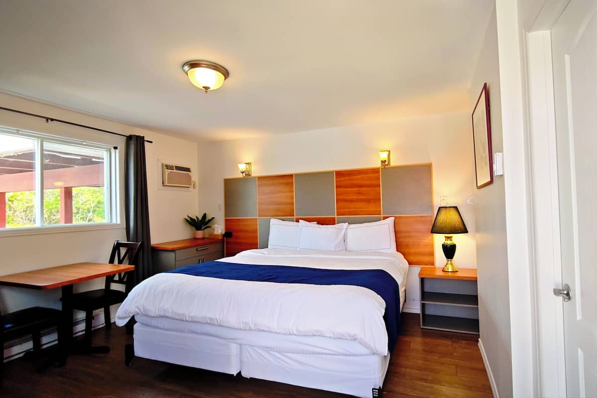 Une chambre d’hôtel comprenant un lit, un bureau, une chaise, une table de chevet, une lampe et une fenêtre avec des rideaux.