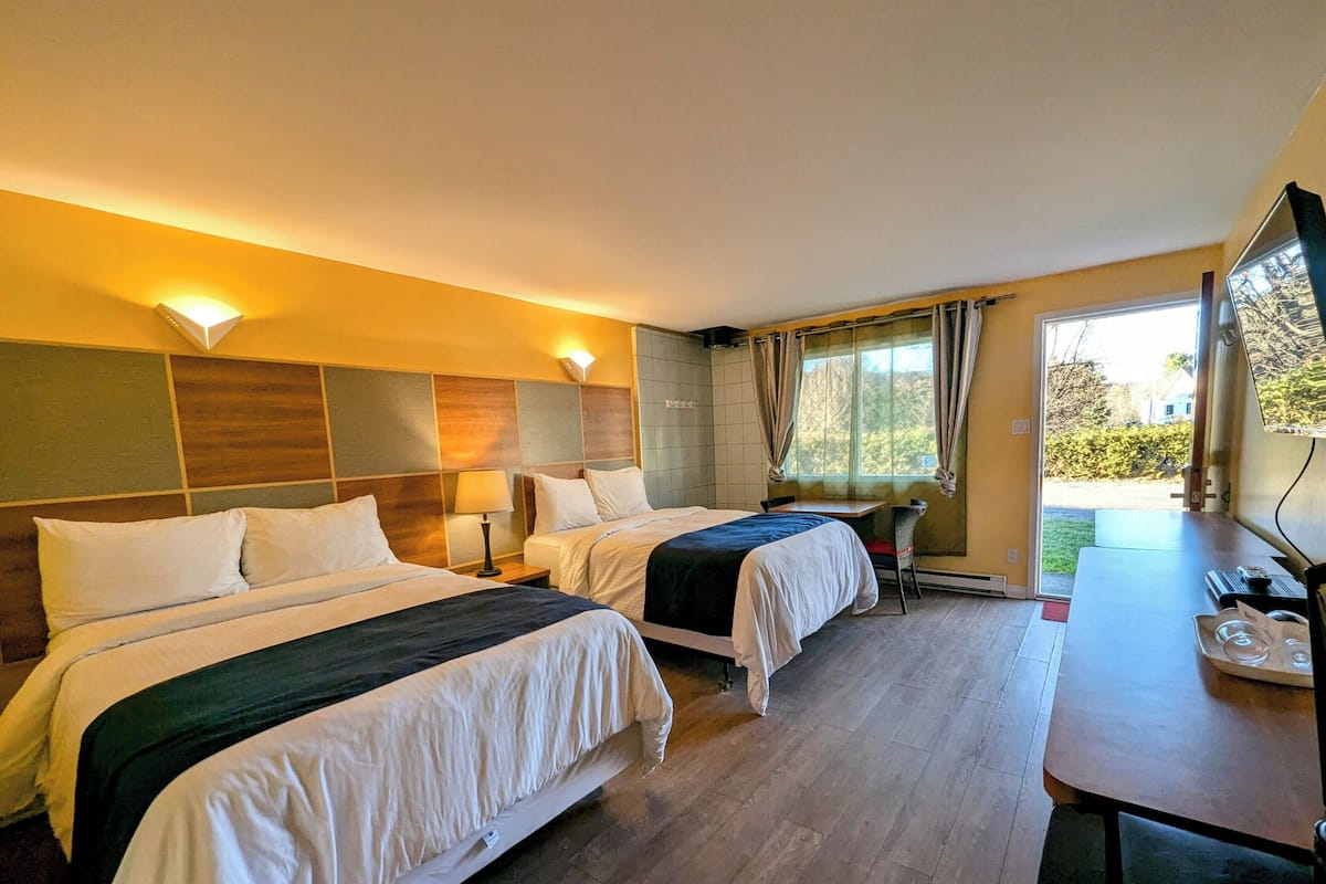 Une chambre d’hôtel avec deux lits, un bureau et une fenêtre avec des rideaux.