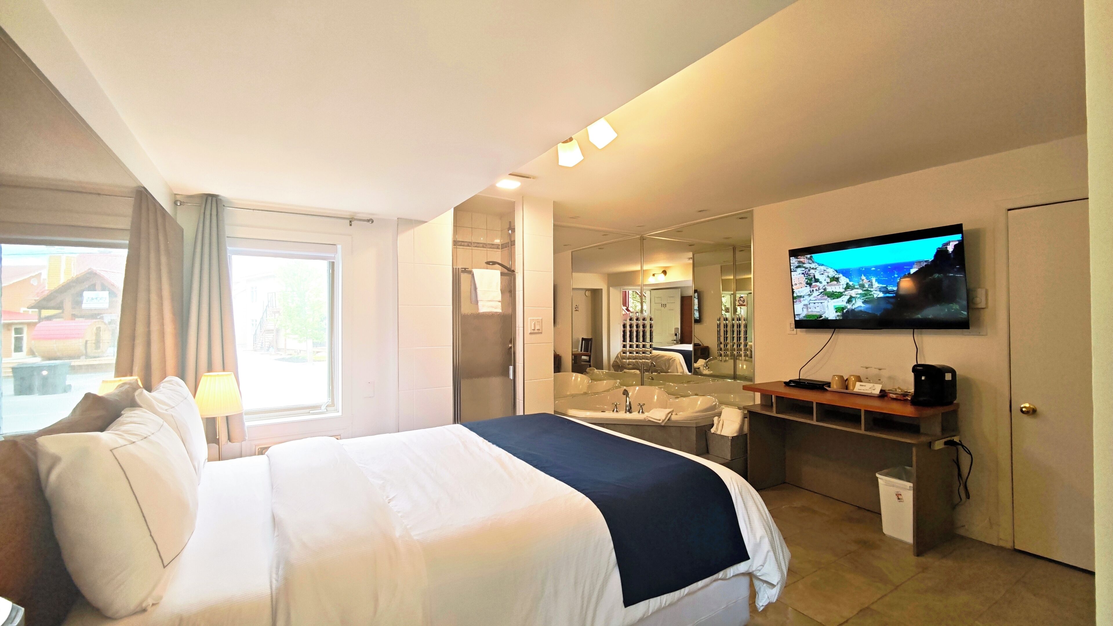 Une chambre d’hôtel avec un lit, une télévision, une salle de bain avec baignoire et une vue sur un bâtiment à l’extérieur.