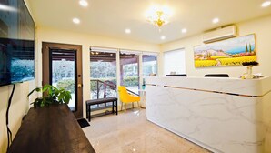 A reception area with a marble counter, a yellow chair, a wooden bench, and a potted plant. - Motel des Pentes et Suites (Saint-Sauveur)