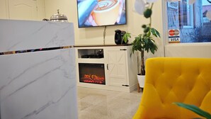 A modern living room with a marble fireplace, a television displaying a coffee cup, and a yellow chair. - Motel des Pentes et Suites (Saint-Sauveur)