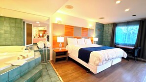 A hotel room with a large bed, a separate bathroom with a bathtub, a desk, and a window with a view of trees. - Motel des Pentes et Suites (Saint-Sauveur)