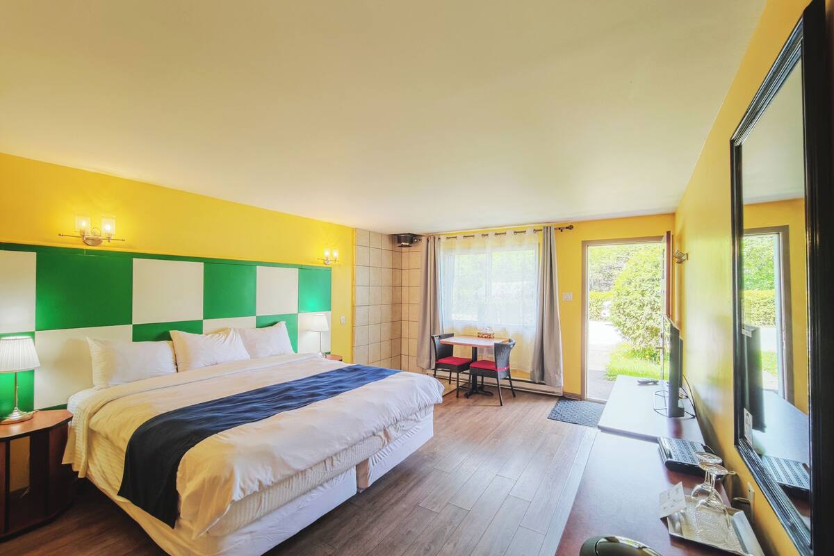 Une chambre d’hôtel avec un grand lit, un bureau avec une chaise, une fenêtre avec des rideaux et une vue sur la verdure.
