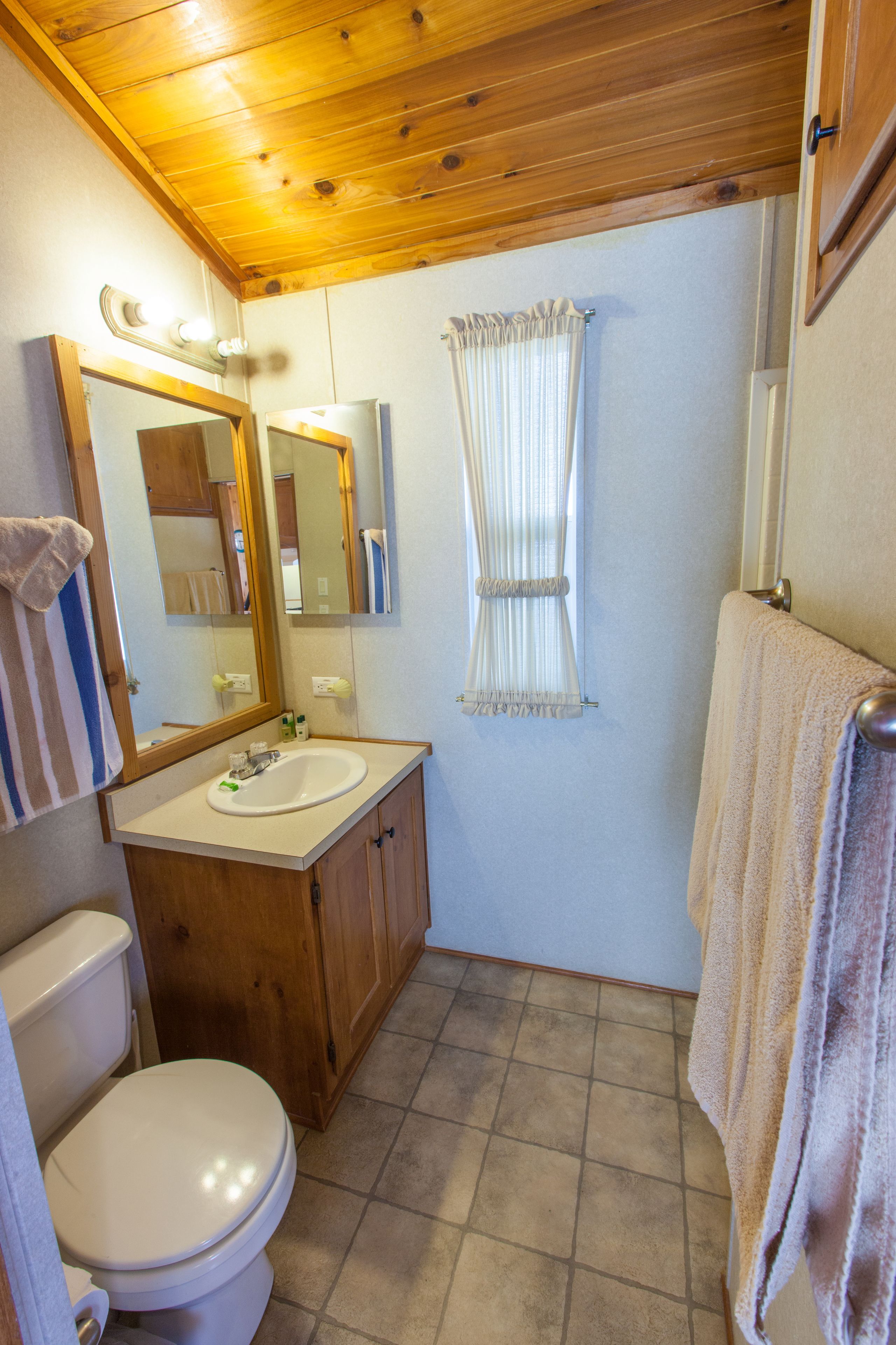A compact bathroom with a wooden vanity, a white sink, a toilet, and a mirror with lights.