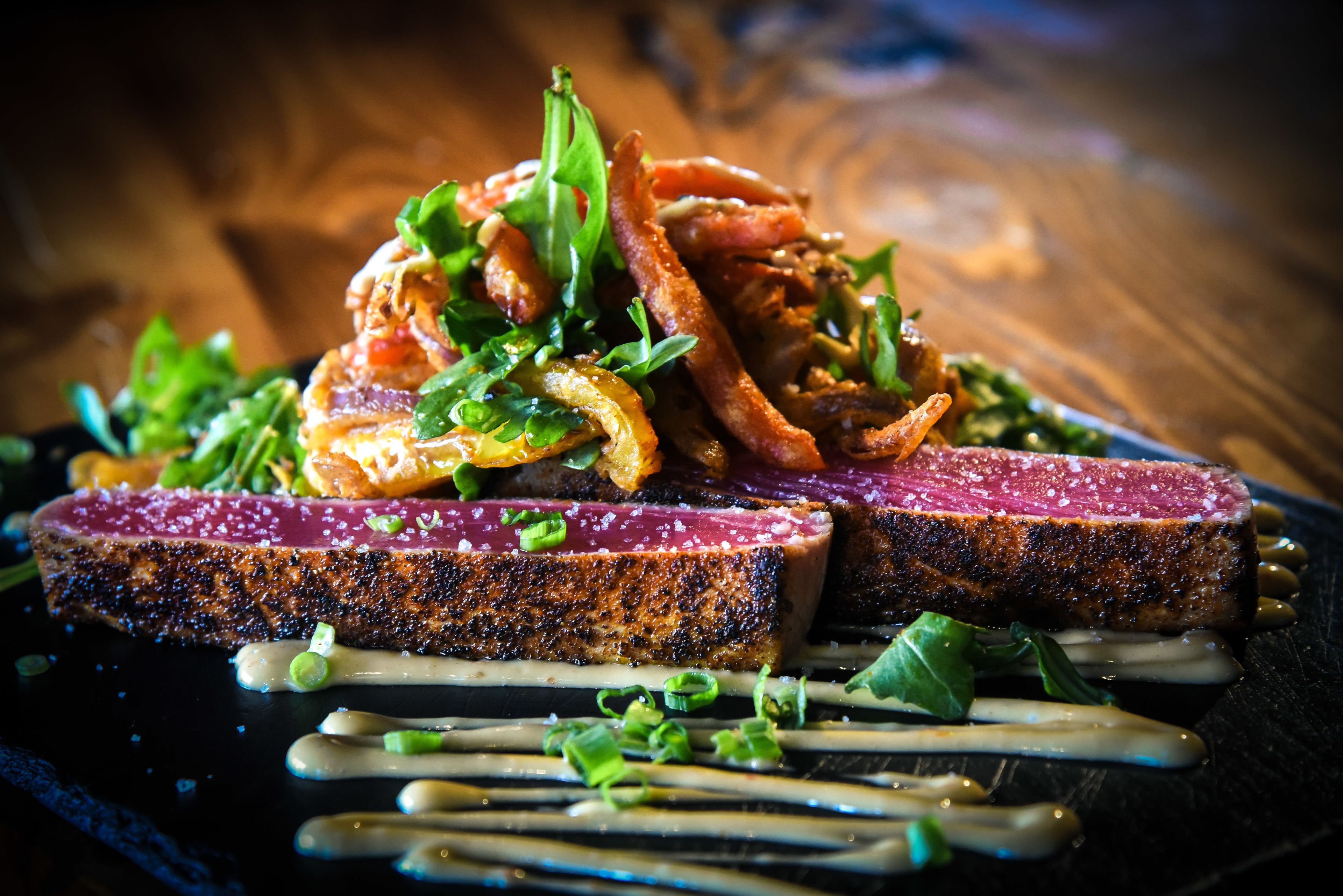 Un steak à la croûte bien dorée, garni d’herbes fraîches et de sauce, servi dans une assiette sombre.