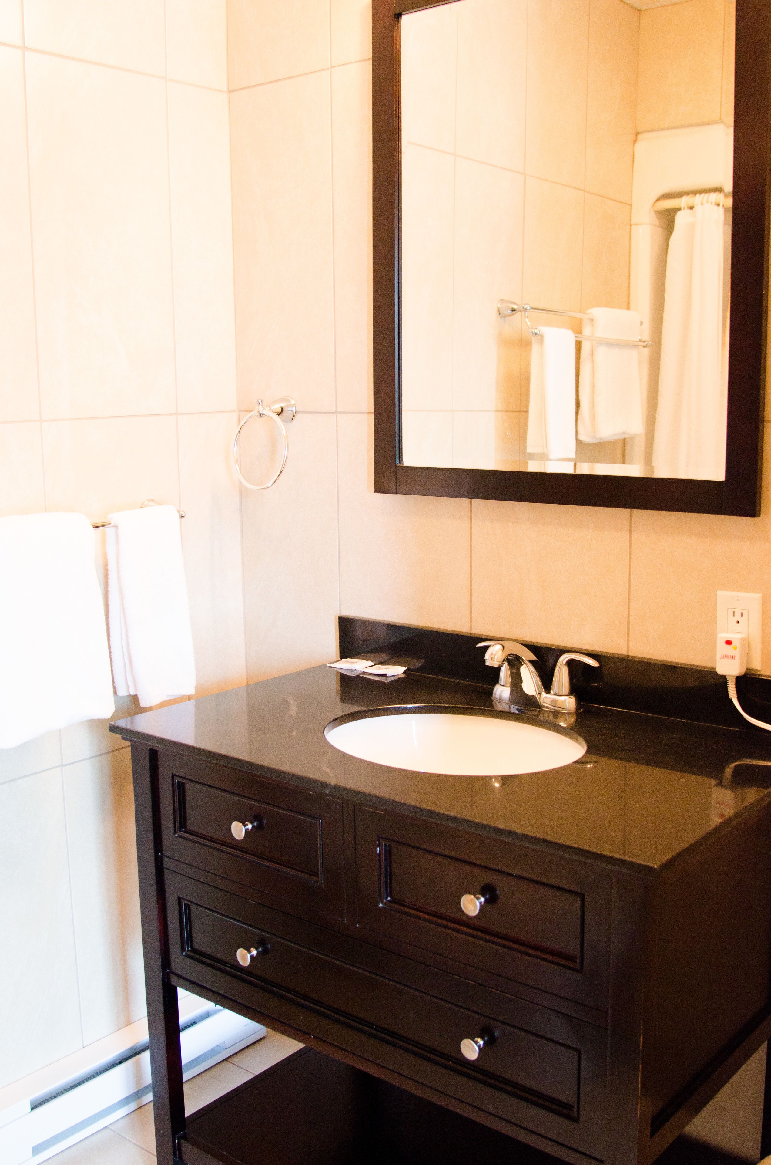 Un baño con tocador oscuro, lavamanos blanco, espejo y toallero.