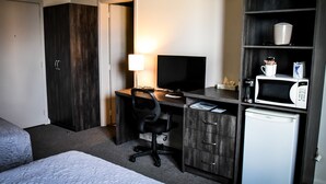 Hotellihuone, jossa on sänky, työpöytä tietokoneella, televisio, mikroaaltouuni ja pieni jääkaappi.