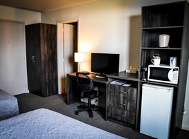 Habitación de hotel con cama, escritorio con computadora, televisión, microondas y refrigerador pequeño.