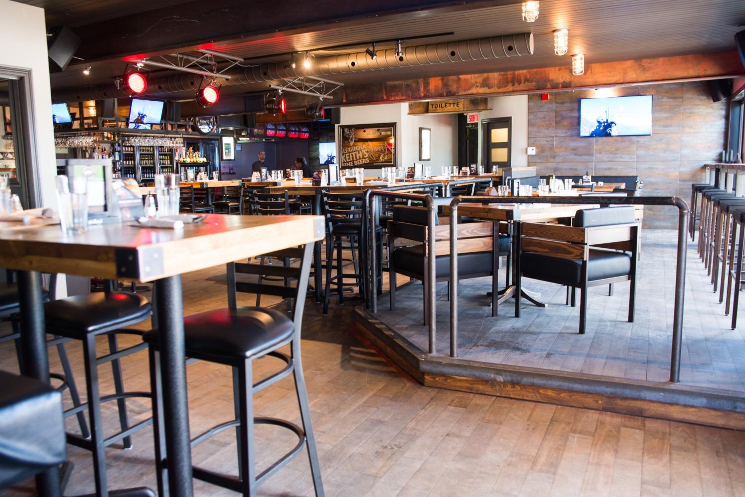 A restaurant with multiple tables and high stools, a bar area, and a visible toilet sign.