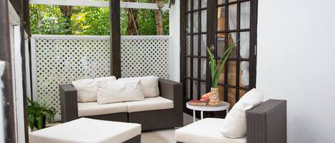 A patio area with wicker furniture, including a sofa and two armchairs, and a small round table with a book and a decorative vase.