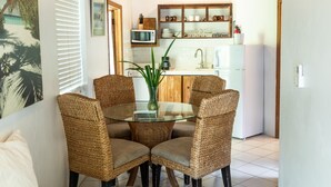 A dining area with wicker chairs and a glass table, a kitchen with white appliances, and a wooden ceiling. - Tingum Village Hotel (Dunmore Town)
