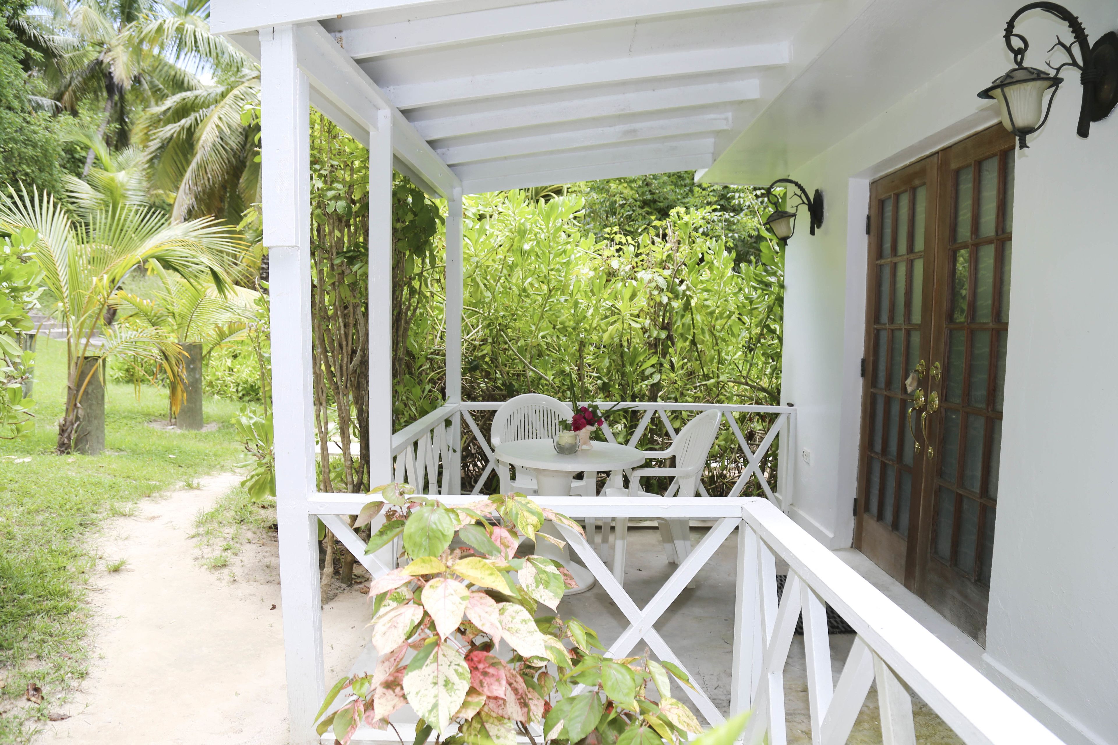 Un patio techado con barandal blanco, una mesa con sillas y una puerta con ventanal.