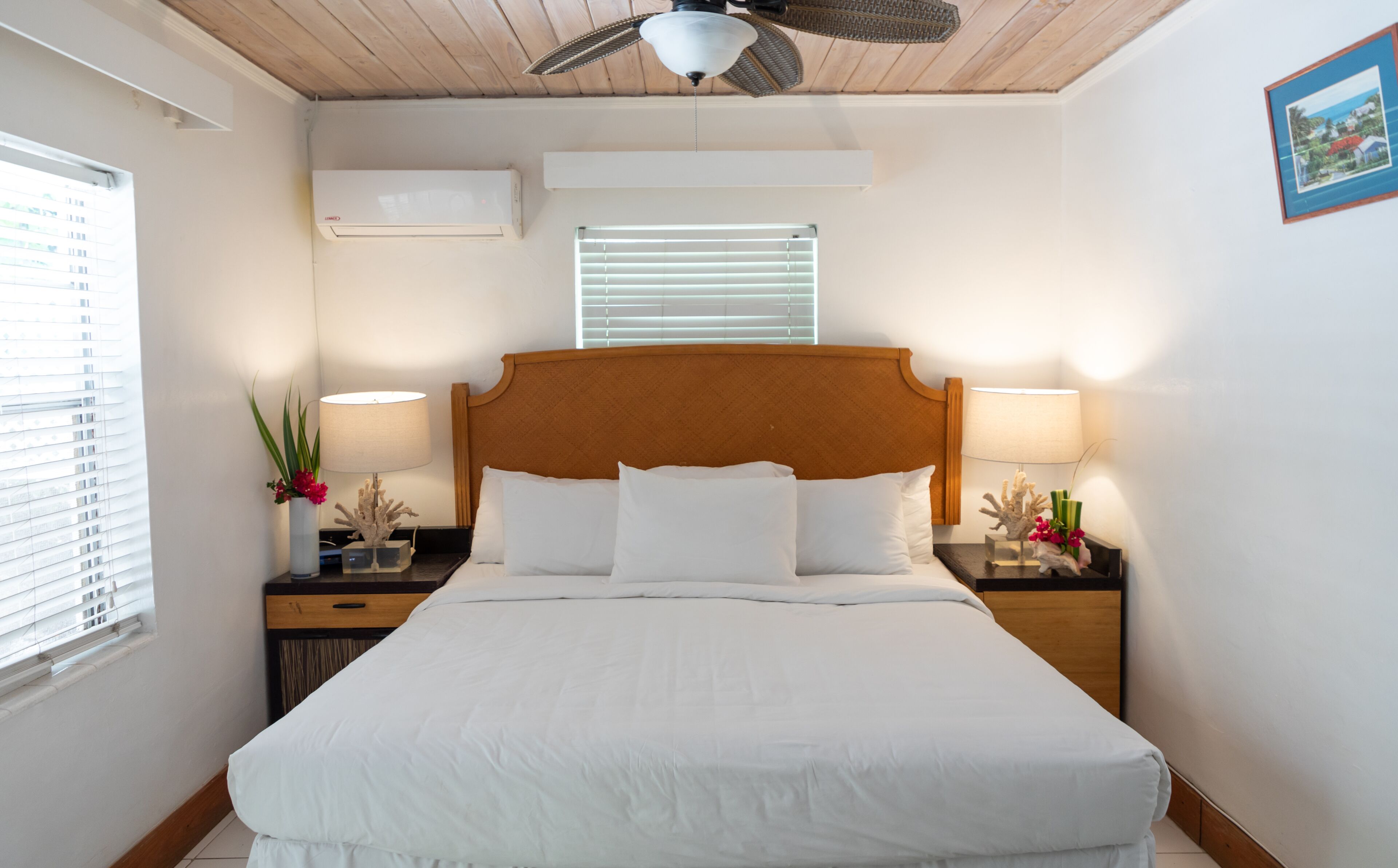A neatly arranged hotel room with a large bed, two bedside tables with lamps, a ceiling fan, and a window with blinds.