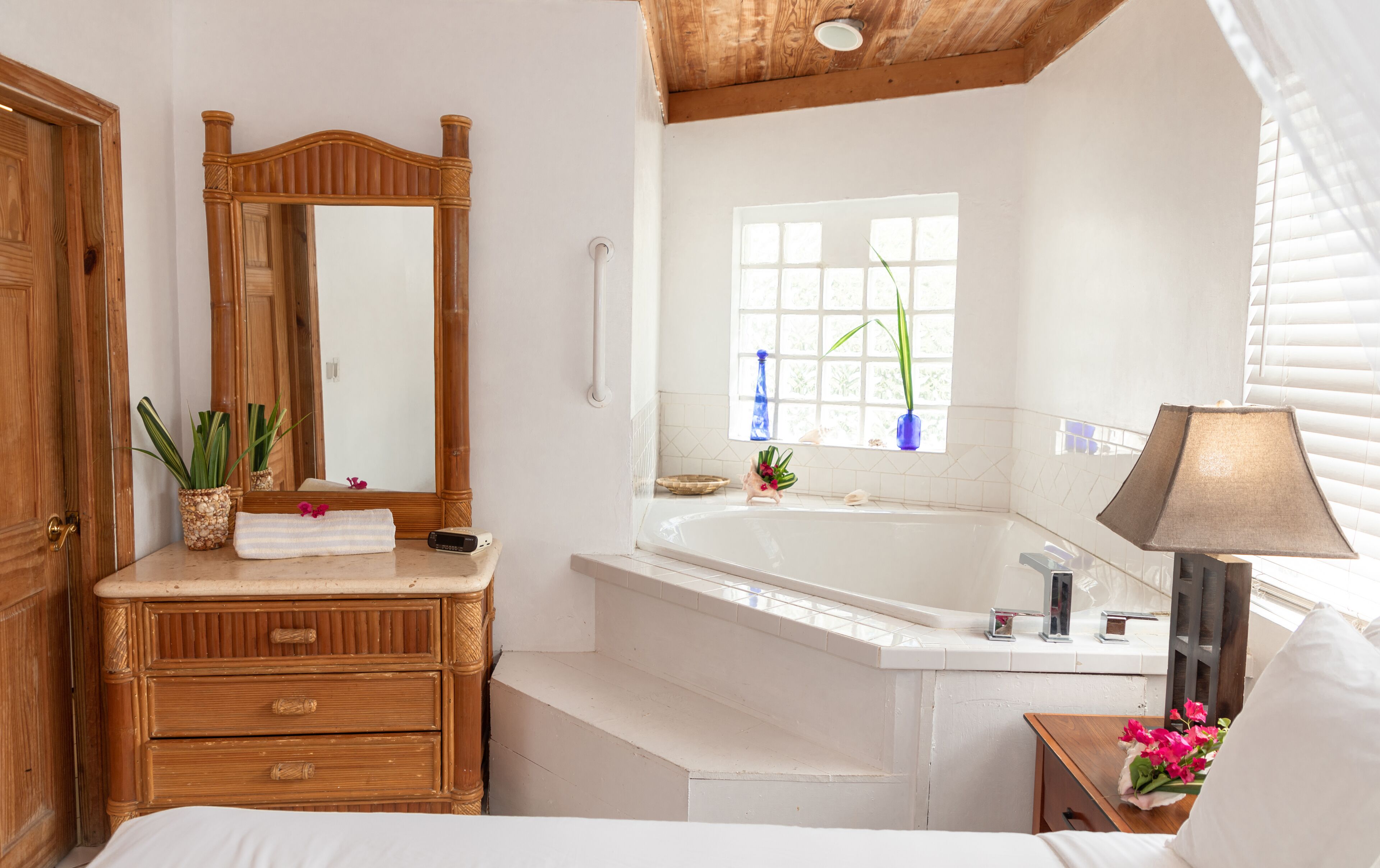 A bathroom with a wooden vanity, a large mirror, a bathtub, and a window with blinds.