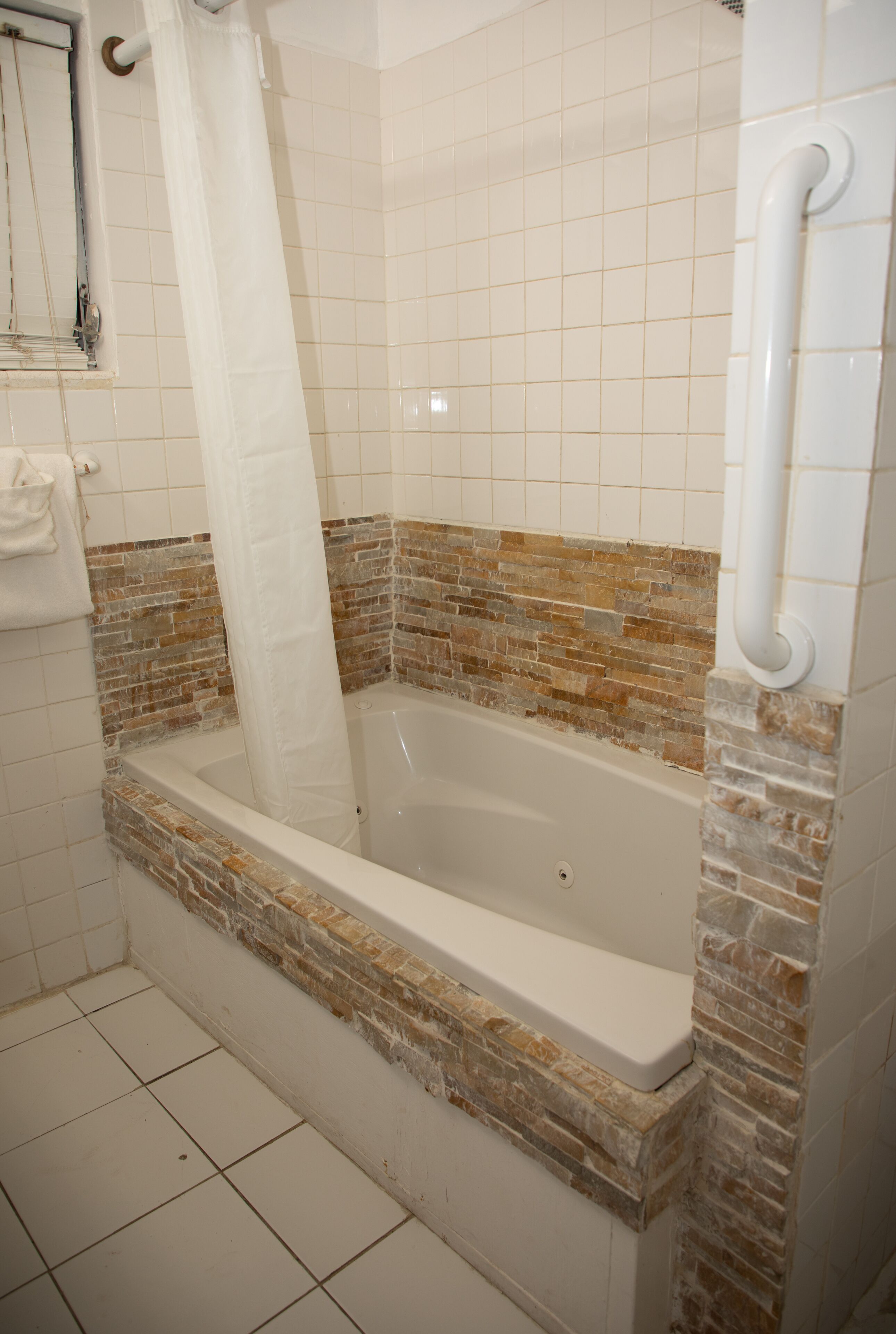 Un baño con bañera, paredes revestidas de azulejos y cortina de ducha.