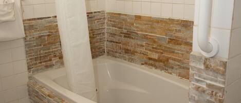 Un baño con bañera, paredes revestidas de azulejos y cortina de ducha.