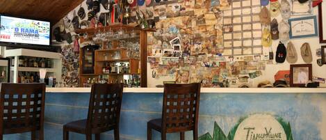 Uma área de bar com cadeiras de madeira e uma parede decorada com diversos chapéus e recordações.