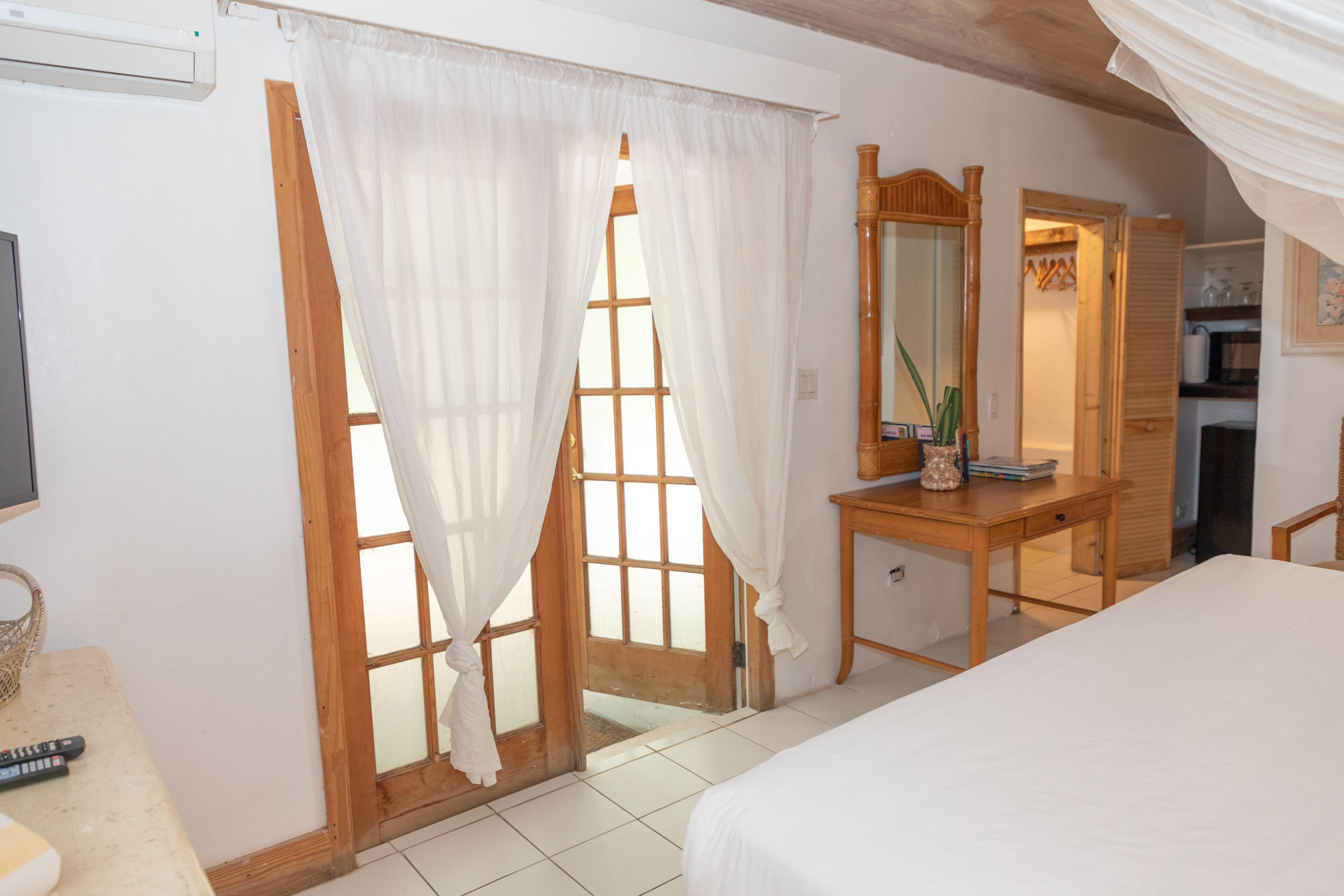 A bedroom with a bed, a wooden desk, a mirror, and a wardrobe.