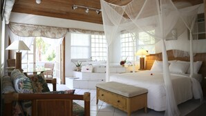 A bedroom with a four-poster bed, a daybed, a sofa, and a small table with a lamp. - Tingum Village Hotel (Dunmore Town)