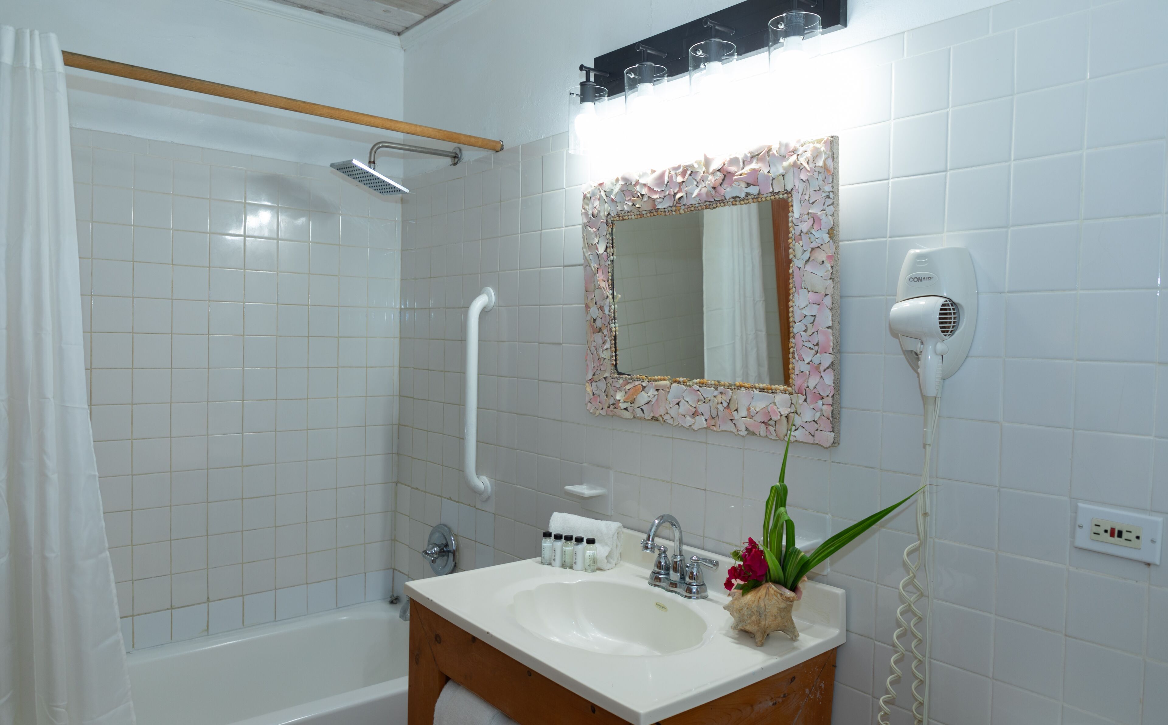 A bathroom with a shower, a sink with toiletries, a mirror, and a hairdryer.