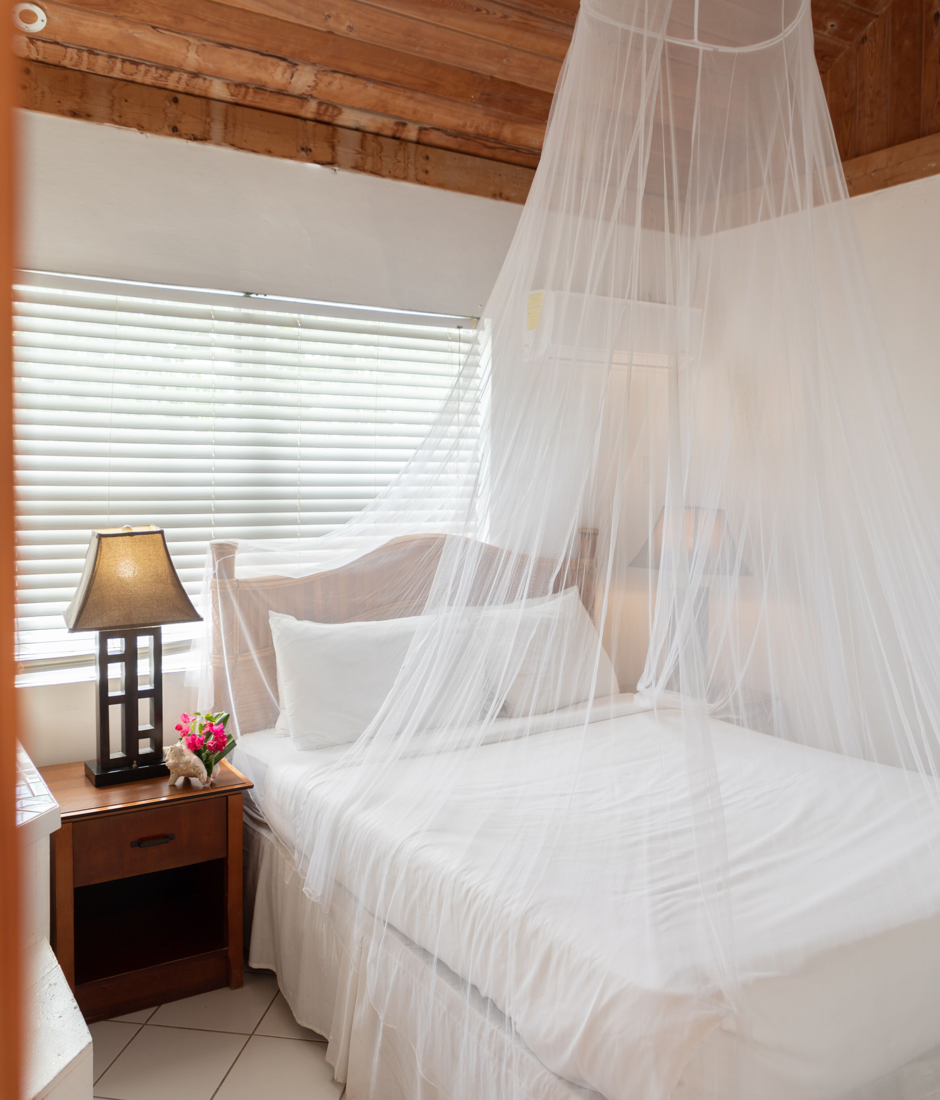 A bedroom with a canopy bed, a bedside table with a lamp, and a nightstand with a drawer.