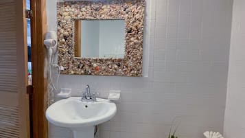 A bathroom with a white sink, a mirror with a pebble frame, and a vanity with toiletries.