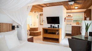 A bedroom with a bed, a TV, a wooden cabinet, and a small kitchen area with a refrigerator and a window. - Tingum Village Hotel (Dunmore Town)
