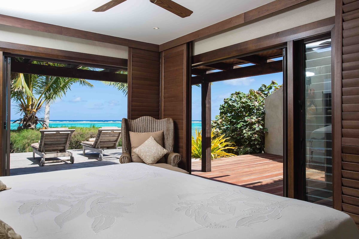 A bedroom with a large bed, a view of the ocean, and a balcony with chairs and a table.