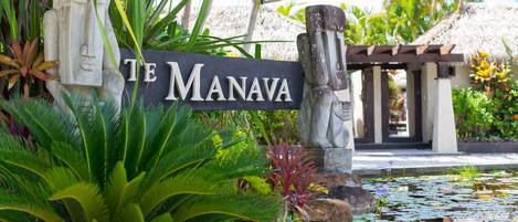 A sign reading "TE MANAVA" with tropical plants and a water feature in the foreground.