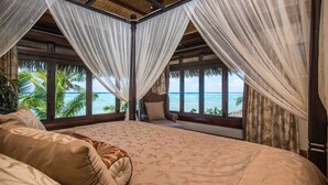 A bedroom with a large bed, a view of the ocean, and a thatched roof.