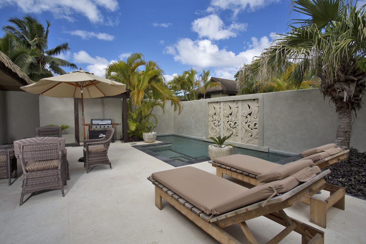 A poolside area with lounge chairs, a dining set, and a decorative wall.
