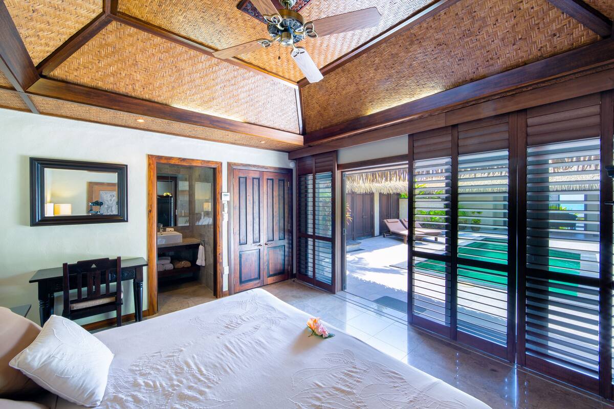 A bedroom with a large bed, a ceiling fan, and a view of a pool through the sliding doors.