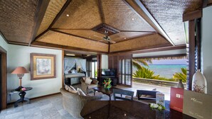 A spacious living area with a large dark marble table, comfortable seating, a ceiling fan, and a view of the ocean.