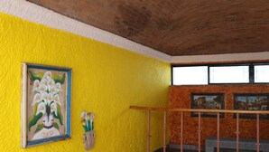 A staircase with a wooden handrail, a yellow wall with a framed painting, and a window with a view of buildings.