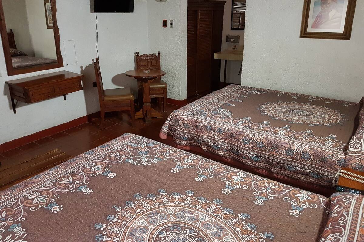 A bedroom with two beds, a wooden dresser, a small table, a chair, a TV, and a mirror.